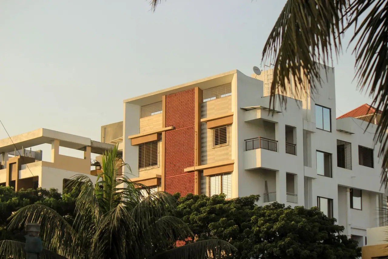 A low-rise apartment building with open balconies, surrounded by palms