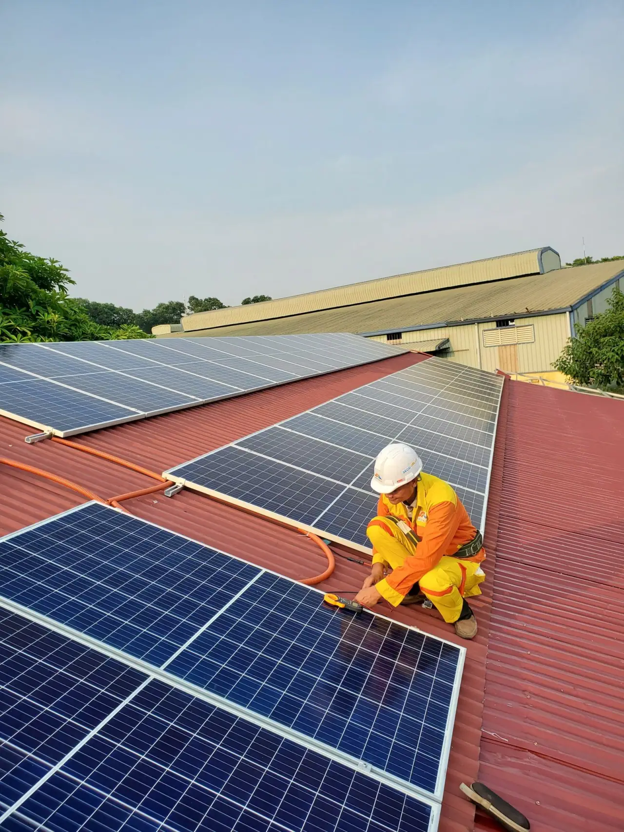 An installer in a helmet, high-visibility vest and gloves working along a rooftop array during commissioning
