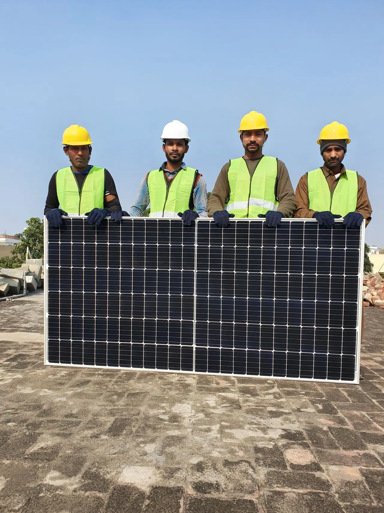 Four installers in high-visibility vests and hard hats carrying a solar module across a rooftop