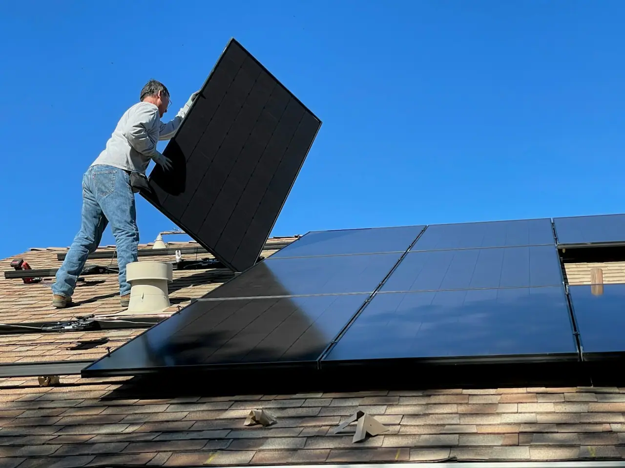 An installer lifting a module into position on a shallow-pitch roof